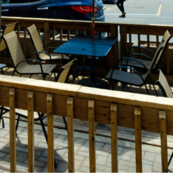 Two streetside patios with guests and a yellow and red umbrella 