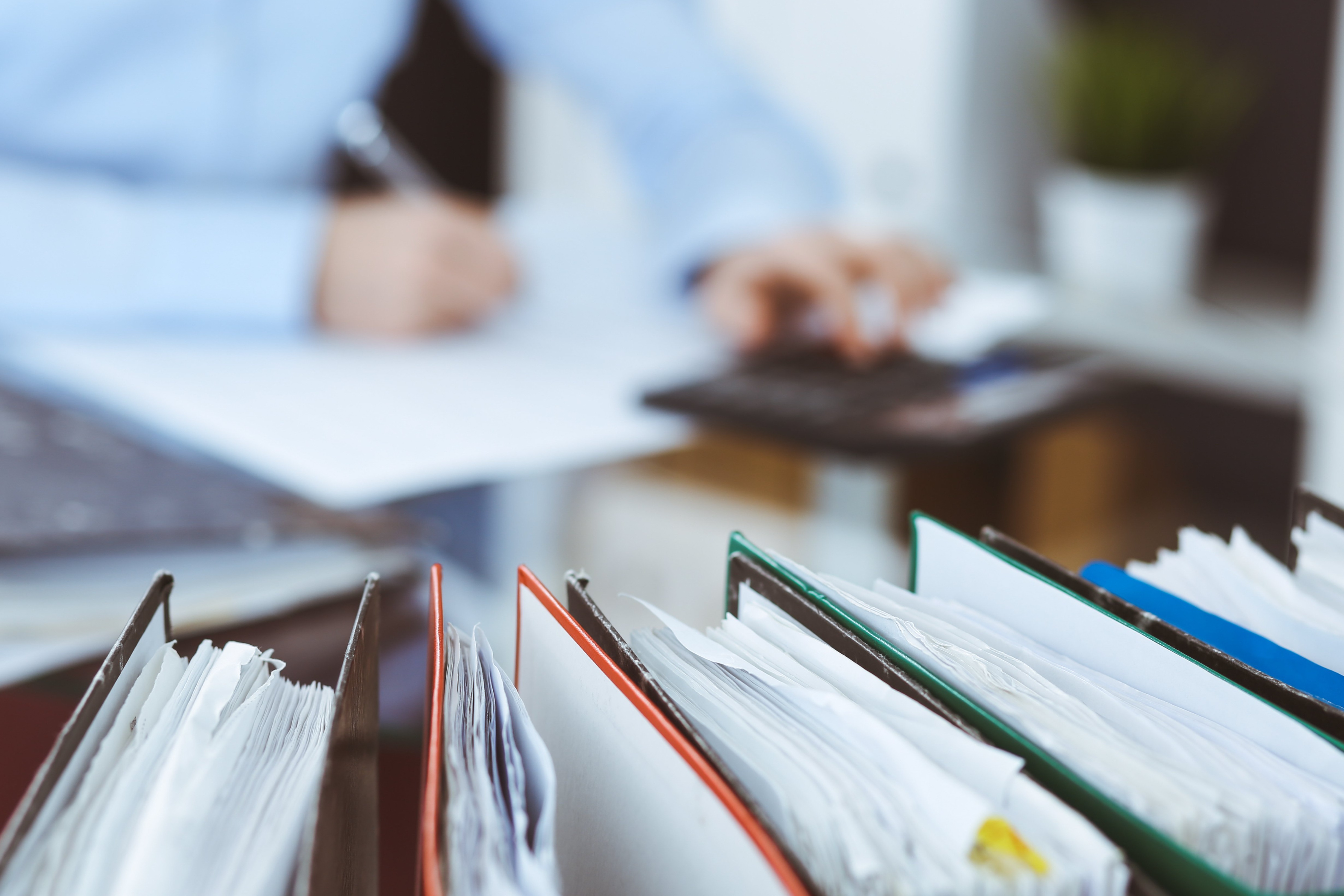 Binders on a desk with a person in the background using a calculator