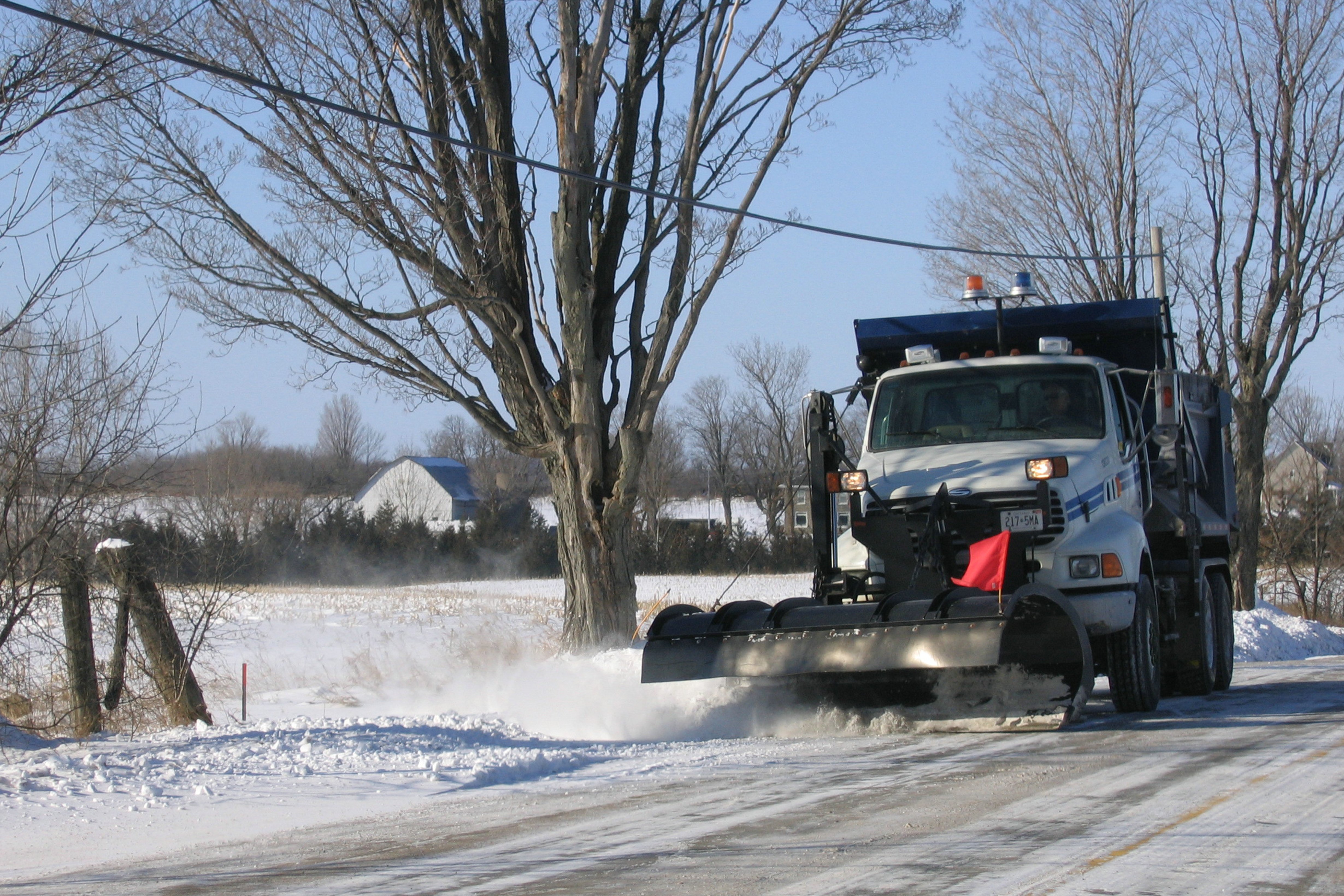 A City snow plow actively plowing a rural City road