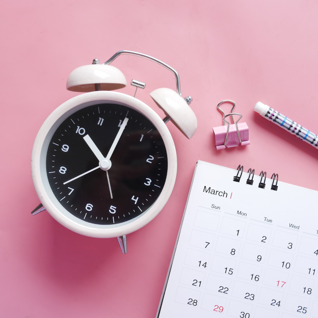 An image with a pink background, white alarm clock, calendar, and pen. 