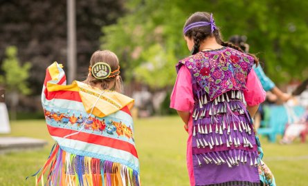 Two children walking away from the camera wearing regalia