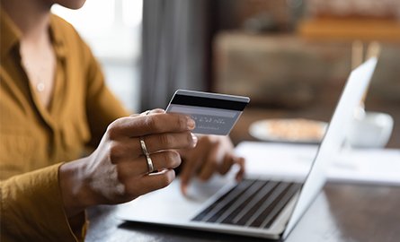 A person holding a credit card in front of a laptop