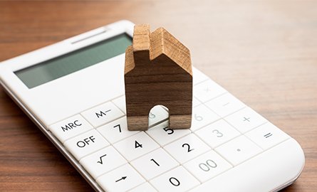 Wooden house token sitting on top of a white calculator