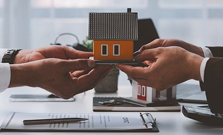 Two people passing a wooden house figurine across a table to one another