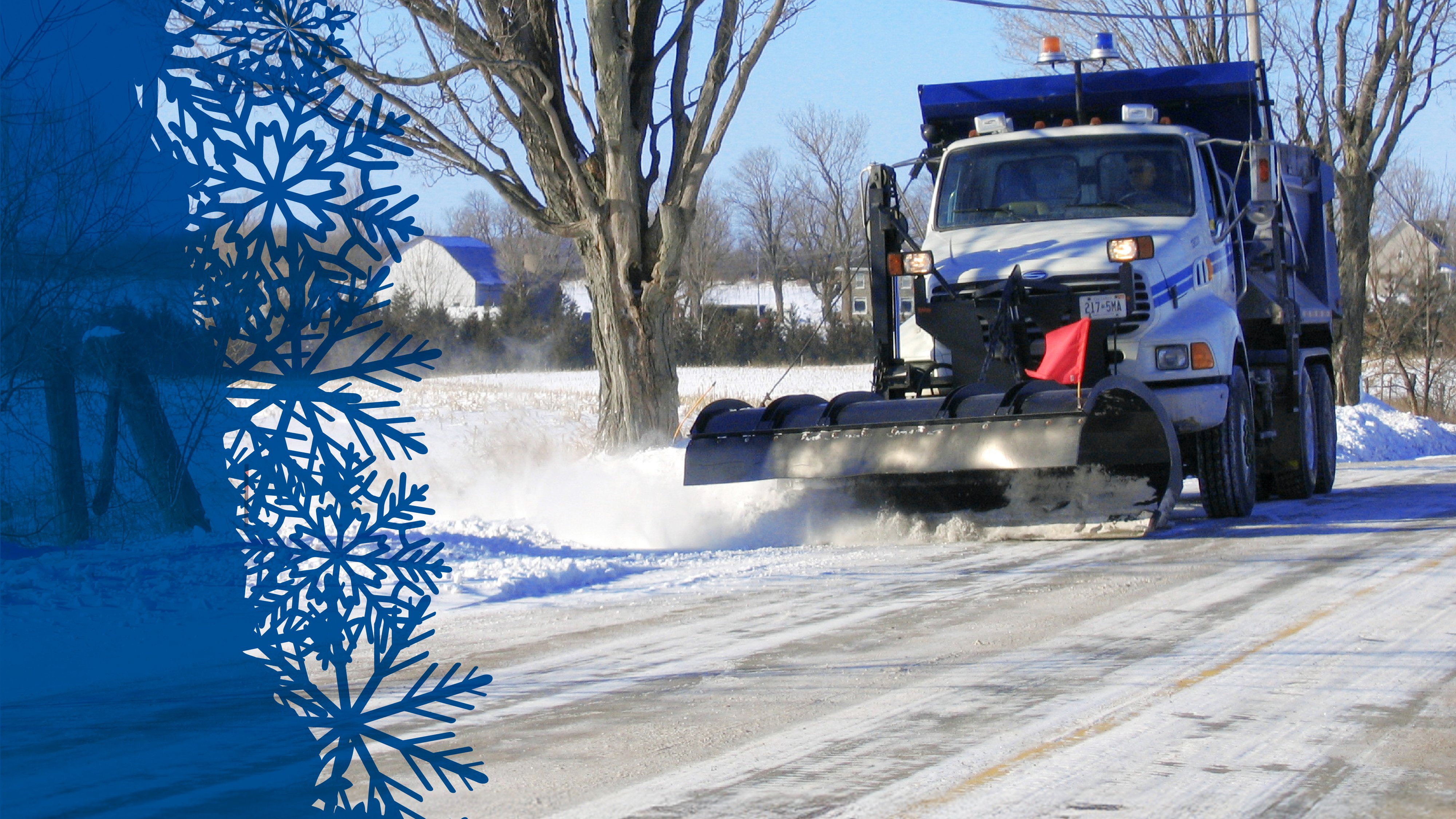 White snowplow drives down snow-filled road. Blue overlay with blue snowflakes on the left side of the photo.