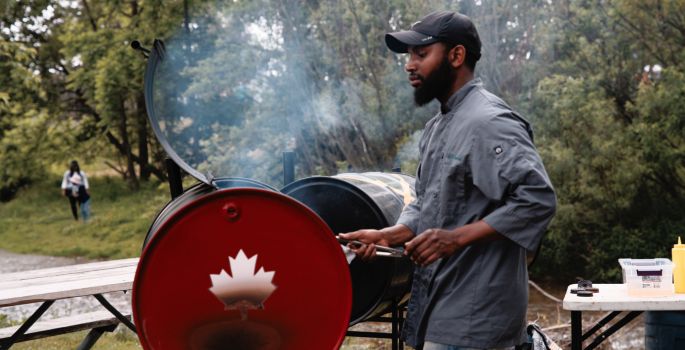 Man grilling with BBQ smoke and large barrel BBQ, up close image