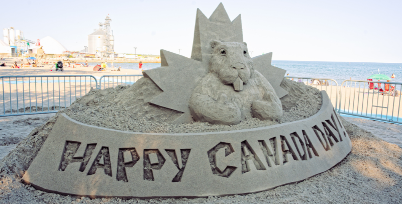 Sand castle creation of a Beaver and Maple Leaf with text reading Happy Canada Day.