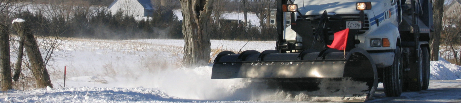 Two yellow snowplows drive down a snowy residential street